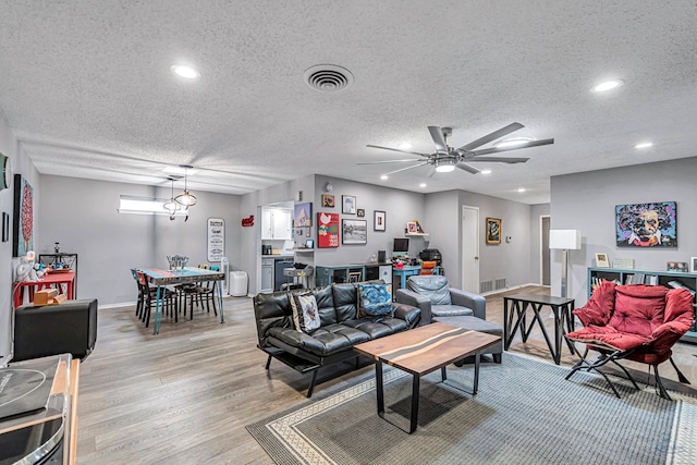 living area with light wood finished floors, visible vents, a textured ceiling, and recessed lighting