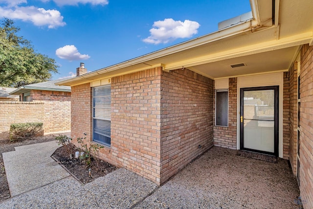 view of exterior entry featuring brick siding, a patio, and fence