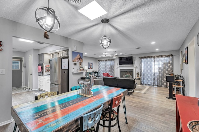 dining area featuring light wood-style floors, ceiling fan, a fireplace, and a textured ceiling