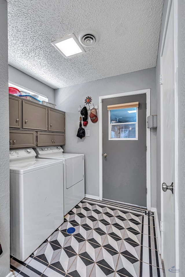 laundry room with a textured ceiling, washing machine and dryer, visible vents, cabinet space, and light floors