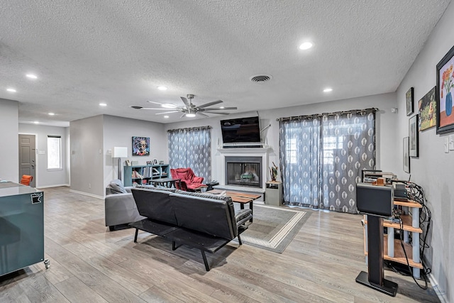 living area with a healthy amount of sunlight, light wood-style flooring, visible vents, and a glass covered fireplace