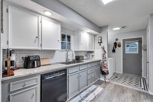 kitchen with black dishwasher, washing machine and clothes dryer, tasteful backsplash, a sink, and light wood-type flooring