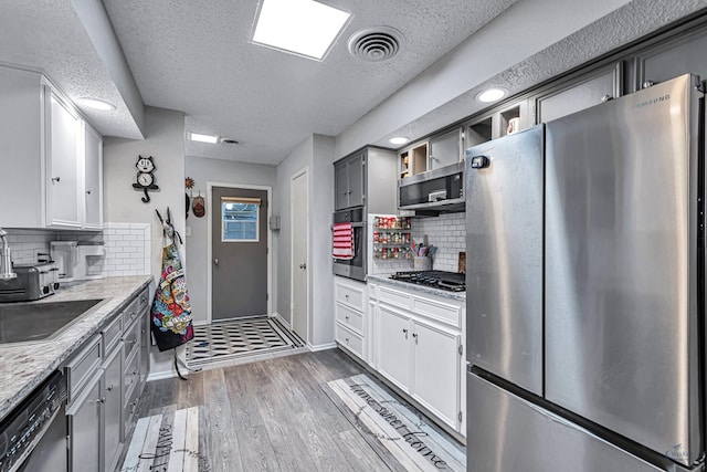 kitchen featuring dark wood-style flooring, visible vents, white cabinetry, appliances with stainless steel finishes, and light stone countertops