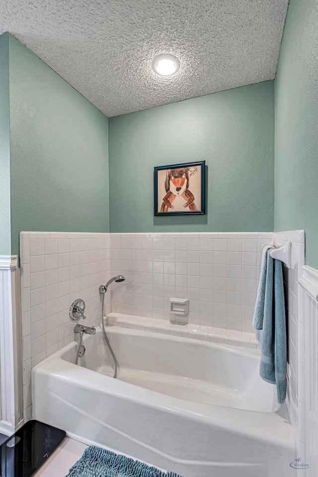 bathroom with a wainscoted wall, a textured ceiling, and a bath