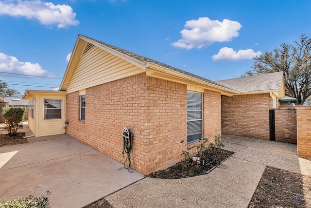 view of property exterior with a patio, brick siding, and a shingled roof