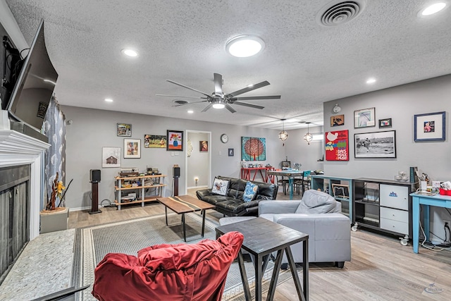 living room featuring light wood-style flooring, visible vents, a fireplace with raised hearth, and a textured ceiling