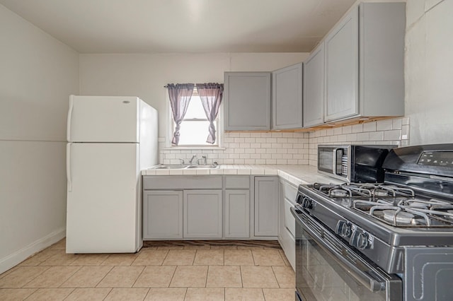 kitchen featuring gas stove, sink, tile countertops, gray cabinets, and white fridge