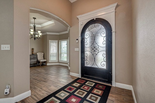 entrance foyer featuring wood finished floors, ornamental molding, arched walkways, baseboards, and a chandelier