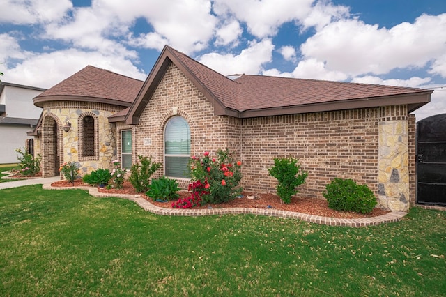 view of front facade with brick siding, a front yard, and roof with shingles