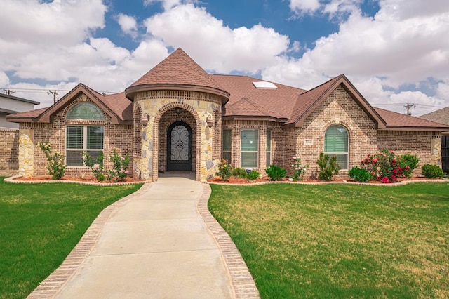french country home with a front lawn, brick siding, and roof with shingles