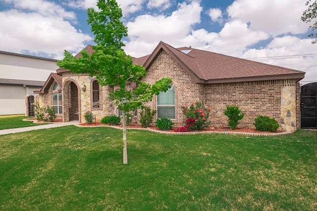 french country home featuring a front lawn, brick siding, and roof with shingles