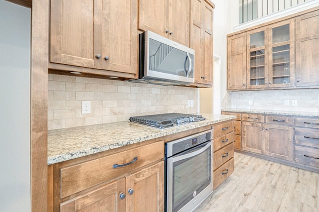 1221 Porterfield Rd, Midland, TX 79705 - kitchen with appliances with stainless steel finishes, backsplash, light wood-type flooring, glass insert cabinets, and light stone countertops