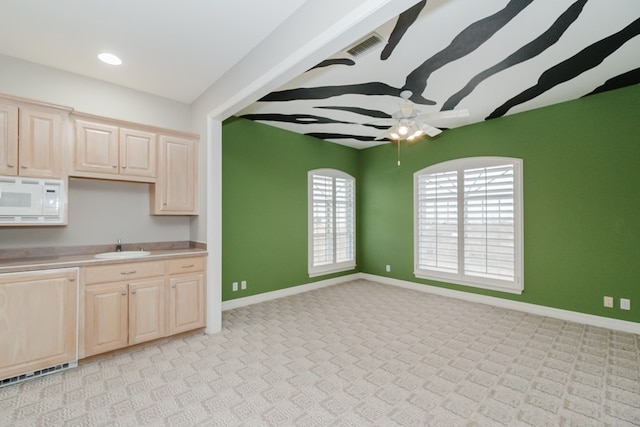 kitchen with light brown cabinets, white microwave, light colored carpet, and sink