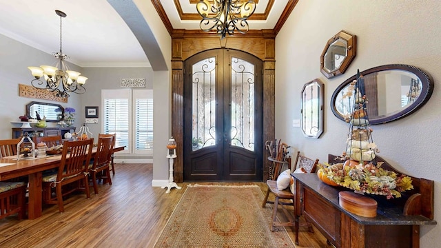 foyer entrance with hardwood / wood-style floors, an inviting chandelier, ornamental molding, and french doors