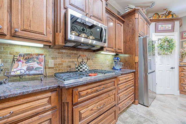 kitchen with appliances with stainless steel finishes, backsplash, ornamental molding, and dark stone countertops