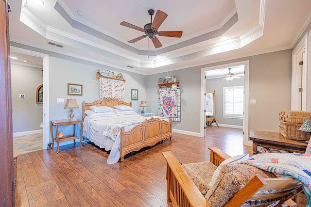 bedroom with hardwood / wood-style floors, ceiling fan, a raised ceiling, and ornamental molding