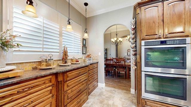 kitchen featuring dark stone counters, double oven, crown molding, a chandelier, and hanging light fixtures