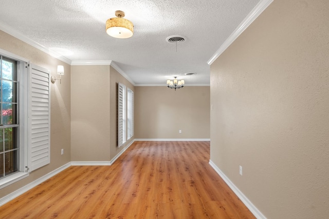 spare room with a textured ceiling, light hardwood / wood-style floors, crown molding, and an inviting chandelier