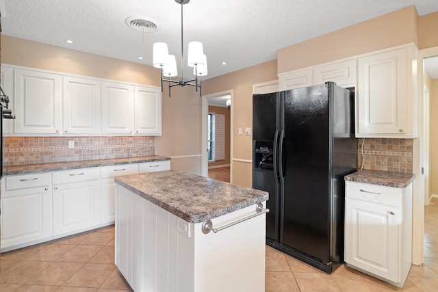 kitchen featuring white cabinetry, a center island, black fridge, backsplash, and decorative light fixtures