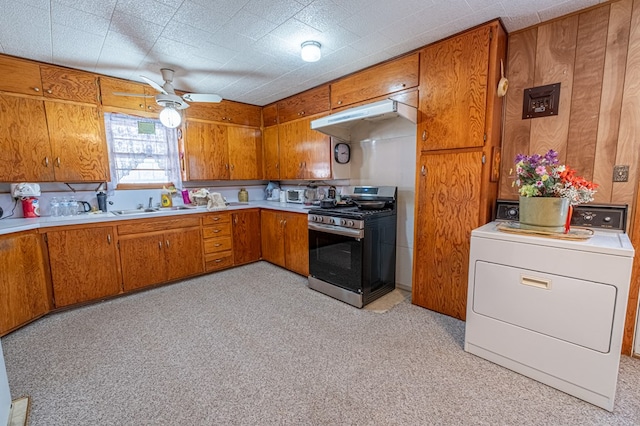 kitchen featuring stainless steel range with gas cooktop, wooden walls, washer / clothes dryer, ceiling fan, and sink