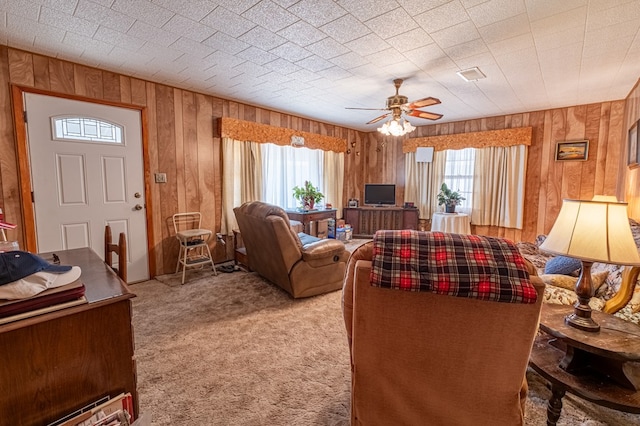 living room with wooden walls, ceiling fan, a healthy amount of sunlight, and light colored carpet