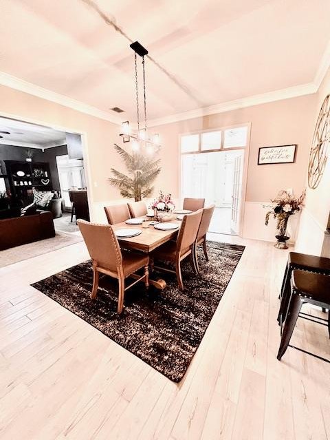 dining room featuring a chandelier, visible vents, ornamental molding, and wood finished floors