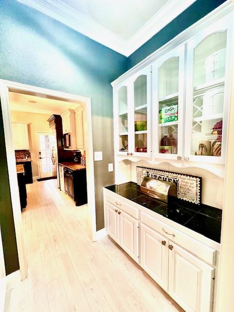bar with backsplash, baseboards, ornamental molding, and light wood-type flooring