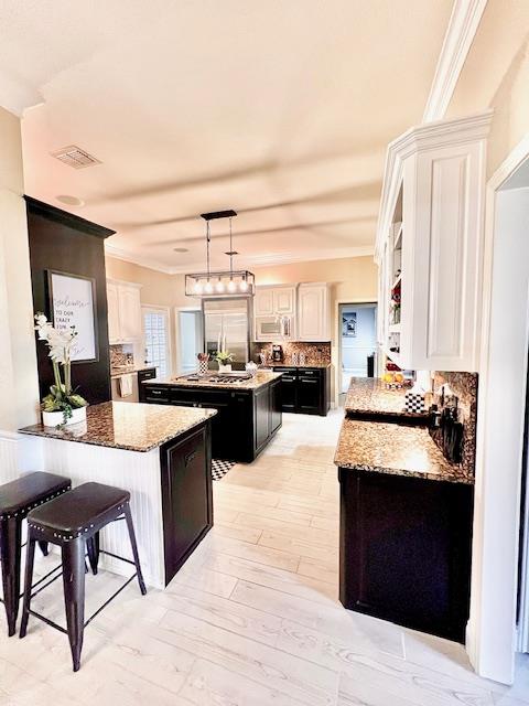 kitchen featuring visible vents, crown molding, a kitchen island, white microwave, and dark cabinets