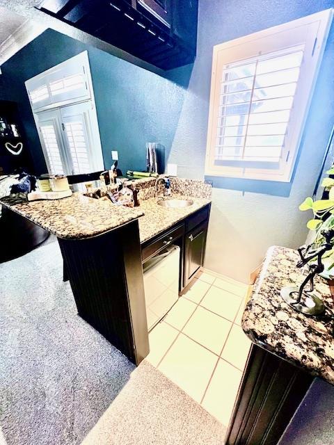 kitchen with a sink, a textured wall, light stone countertops, and light tile patterned flooring