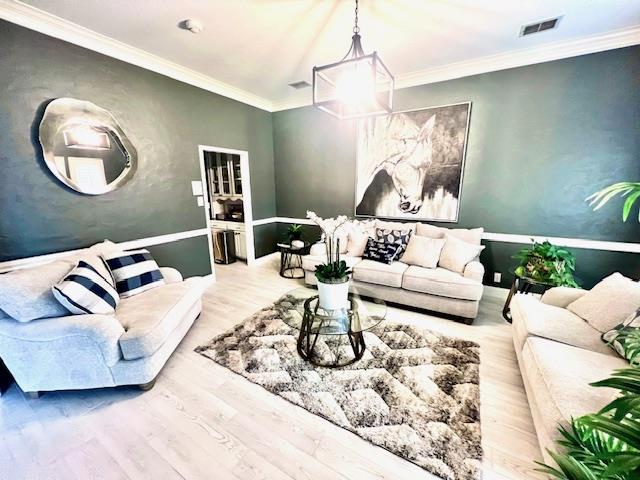 living room with crown molding, wood finished floors, a chandelier, and visible vents