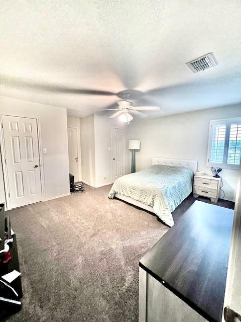 bedroom featuring ceiling fan, a textured ceiling, visible vents, baseboards, and carpet floors