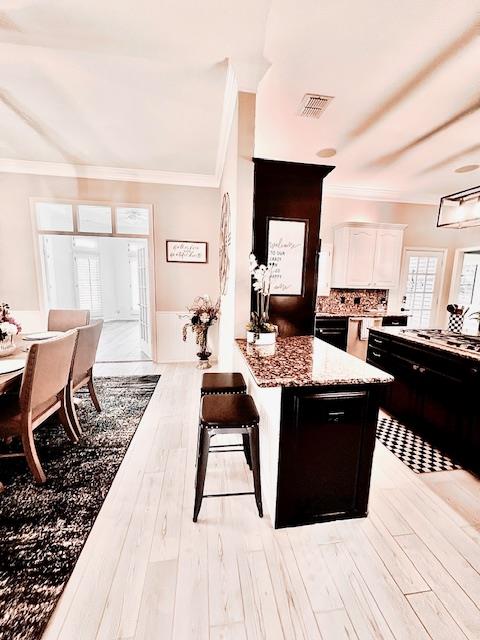 kitchen with ornamental molding, a peninsula, light stone countertops, light wood-style floors, and white cabinetry