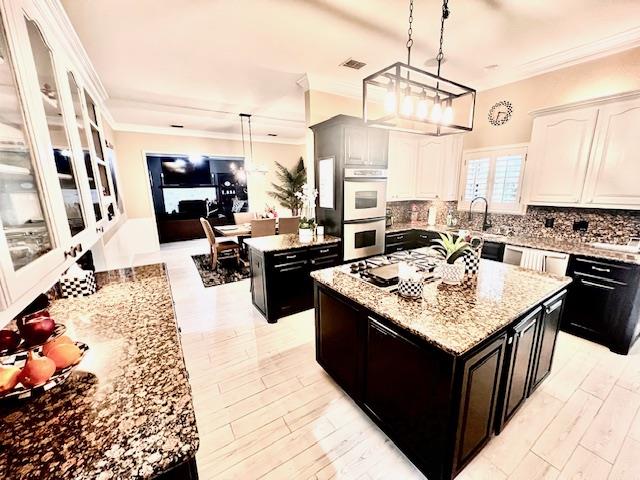 kitchen with backsplash, a center island, double oven, ornamental molding, and white cabinetry