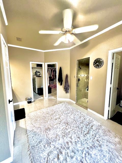 bedroom with a ceiling fan, visible vents, tile patterned flooring, connected bathroom, and ornamental molding