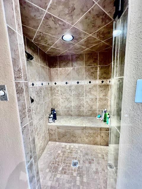 bathroom with a textured wall and a tile shower