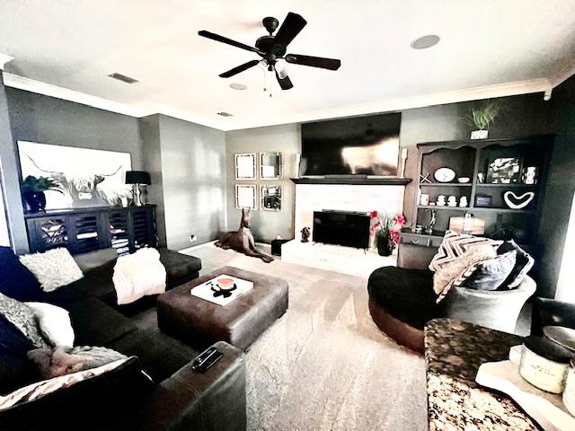 carpeted living area with crown molding, a ceiling fan, visible vents, and a fireplace