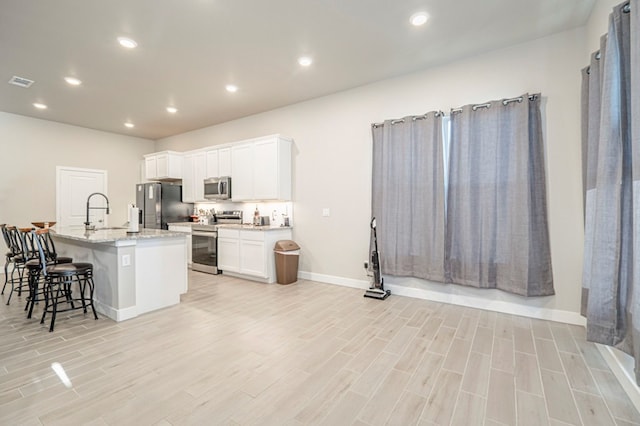 kitchen with visible vents, white cabinets, an island with sink, a breakfast bar area, and stainless steel appliances