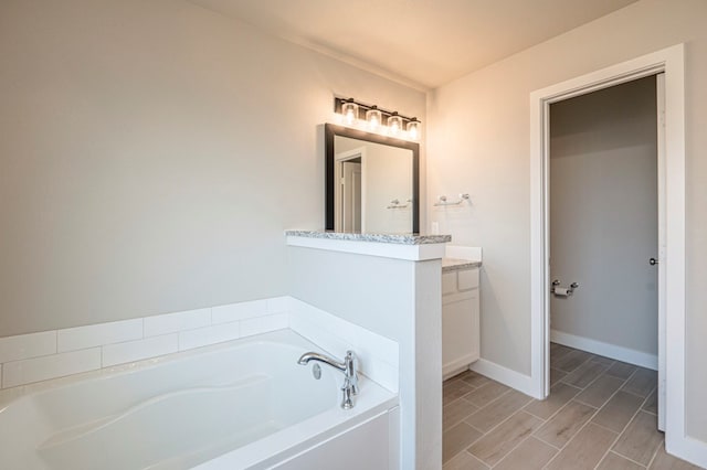 bathroom with a garden tub, wood tiled floor, baseboards, and vanity