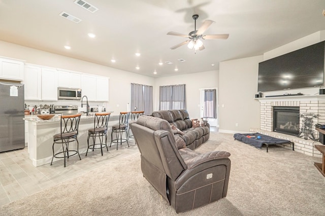 living area featuring a ceiling fan, visible vents, a fireplace, and light carpet