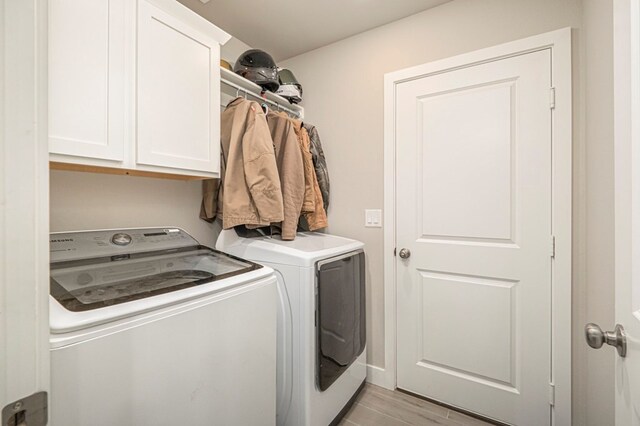 clothes washing area with light wood-type flooring, cabinet space, and independent washer and dryer