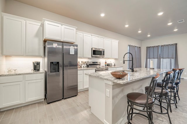 kitchen featuring visible vents, white cabinets, a kitchen island with sink, stainless steel appliances, and a sink