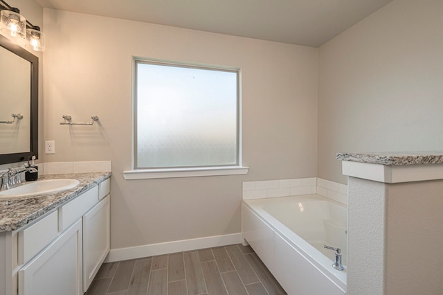 full bath featuring wood tiled floor, a garden tub, vanity, and baseboards