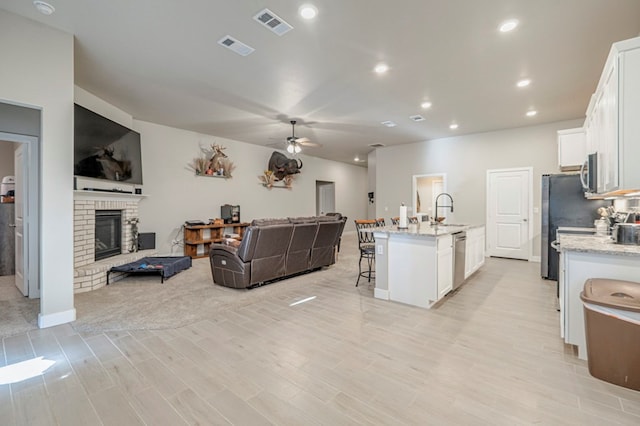 living area with light wood-style flooring, recessed lighting, visible vents, a ceiling fan, and a brick fireplace