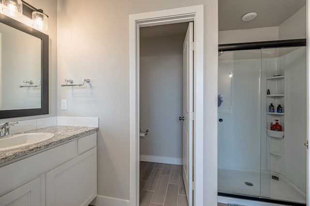 bathroom featuring a shower stall, vanity, baseboards, and wood finish floors