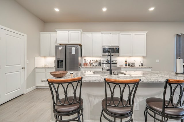 kitchen featuring light stone counters, appliances with stainless steel finishes, white cabinets, and a sink