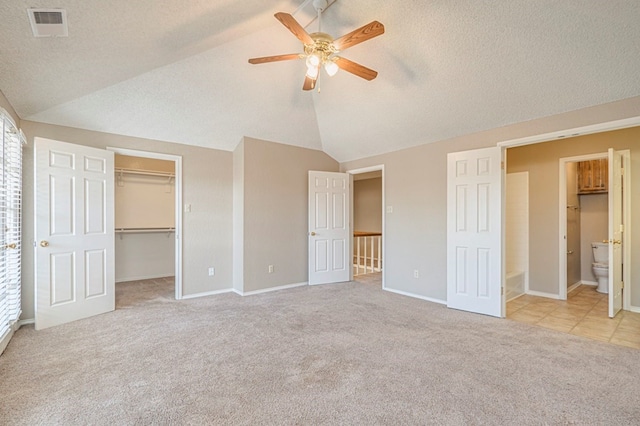 unfurnished bedroom with connected bathroom, a textured ceiling, light carpet, a spacious closet, and vaulted ceiling