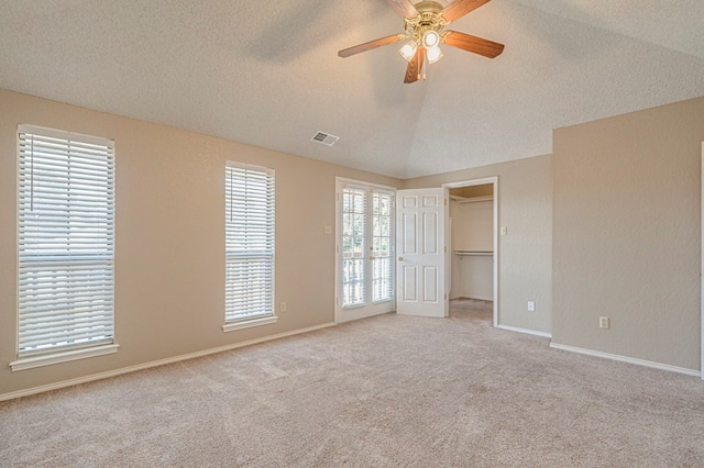 unfurnished bedroom featuring a walk in closet, light colored carpet, vaulted ceiling, a textured ceiling, and ceiling fan