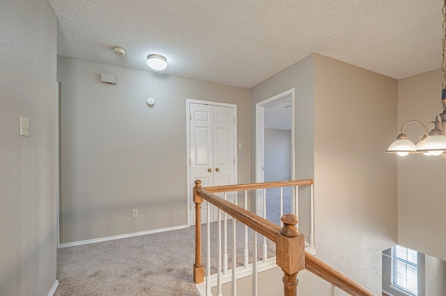 corridor with a notable chandelier, carpet floors, and a textured ceiling