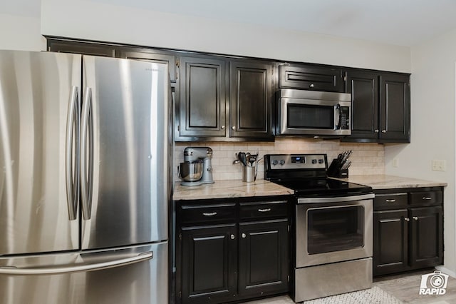 4313 Downing Ave, Midland, TX 79707 - kitchen with stainless steel appliances, dark cabinets, backsplash, light stone countertops, and light wood-style flooring