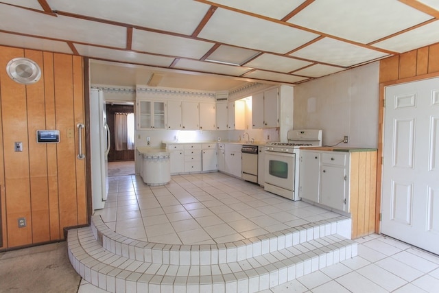 kitchen featuring wood walls, light tile patterned floors, white cabinets, and white appliances